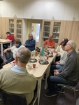 Kolem stolu s občerstvením sedí několik mužů a žen