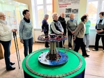 Na obrázku návštěvníci při výkladu v místnosti, kde ve středu je model pouťového kolotoče 