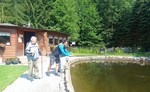 Na obrázku dva muži, jeden chytá v jezírku ryby a druhý ho sleduje.