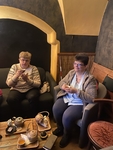 Dvě ženy s šálky čaje v rukou sedí u malého stolku s čajovými soupravami.