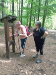 Dvě z nás stojící před dřevěnou tabulí - součást turistické trasy - a zkouší splnit úkol.