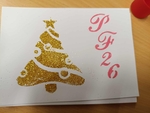 Na fotografii je novoroční přání v jehož levé části se nachází stylizovaný pozlacený vánoční stromeček. V pravé části je velkým písmem růžový nápis PF 26 