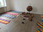 Na fotografii jsou na podlaze rozložené pestrobarevné podložky na cvičení a také rozličné hudební nástroje a pomůcky na muzikoterapii, například gong a tibetské mísy 